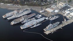 An aerial view of the Puget Sound Naval Shipyard and Intermediate Maintenance Facility in Bremerton, Wash. (USA), on November 24, 2012. Visible are the following ships (top to bottom): aircraft carrier USS Independence (CV-62); USS Kitty Hawk (CV-63); USS Constellation (CV-64); amphibious transport dock ship USS Dubuque (LPD-8); USS Ranger (CV-61); three Oliver Hazard Perry-class frigates; an (active) Lewis and Clark-class dry cargo ship; a Seawolf-class submarine. (Credit: Jelson25 - Own work)