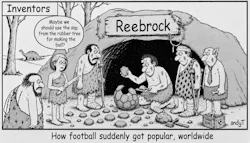 Black-and-white cartoon titled “Inventors.” A group of injured prehistoric people stands outside a cave labeled “Reebrock,” with a cavewoman suggesting, “Maybe we should use the sap from the rubber tree for making the ball?” In front of the cave, a man kneels holding a trowel with mortar and a stone facet as he assembles a stone soccer ball made of hexagonal and pentagonal panels. The group is on crutches, and has leg casts and bandages and head bandages.The caption at the bottom reads, “How football suddenly got popular, worldwide.”